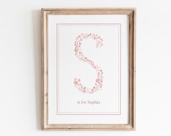 May include: A framed print with a floral letter S in pink and white. The text "S is for Sophia" is below the letter.