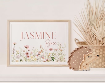 May include: A framed print with the name "JASMINE Renee" in a soft pink font, surrounded by watercolor flowers. A wooden hedgehog night light with small lights sits beside a woven basket with dried plants. The scene is set on a white dresser.