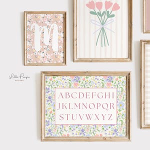 May include: A collection of framed floral art prints. One print features the letter "M" in white over a floral pattern. Another displays a bouquet of pink flowers. A third print has the alphabet in a pink box.