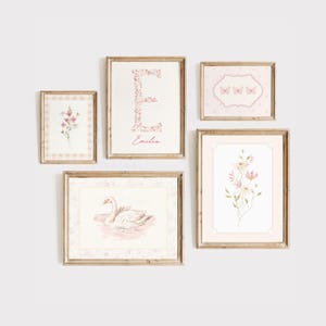 May include: Five framed prints with a pink and white floral theme. The prints feature a swan, butterflies, flowers, and a floral letter E with the name "Emilia" written below. The frames are all a light wood color.