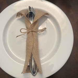 May include: A white plate with a fork and knife wrapped in burlap and tied with twine.