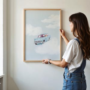May include: A framed painting of a blue car driving through clouds. The painting is hanging on a white wall. A person is hanging the painting on the wall.