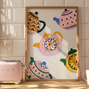 Puede incluir: Una lámina de arte mural enmarcada que presenta una colección de cinco teteras coloridas con diversos patrones y tonos, incluyendo naranja, rosa y amarillo, sobre un fondo crema. Las teteras muestran formas geométricas, motivos florales y rayas.