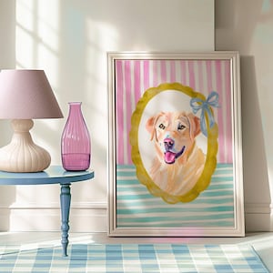 May include: A framed dog portrait with a golden retriever inside an oval frame with a gold border and a blue bow. The background has pink and white stripes above blue and white stripes. A pink lamp and vase sit on a blue table.