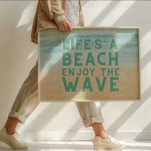 Könnte beinhalten: Ein weißer gerahmter Druck mit einer Strandszene und dem Text "Life's a Beach Enjoy the Wave" in grüner Schrift.