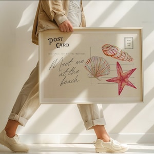 Op de afbeelding: Een ingelijste ansichtkaartprint met een strandthema. De print bevat illustraties van een zeeschelp, een zeester en een zeeslak. De tekst luidt "Meet me at the beach" en "Post Card". De lijst is wit.