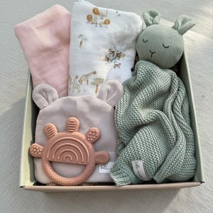 Puede incluir: Un set de regalo para bebé en una caja, con una manta de muselina rosa, una manta blanca con estampado de safari, una manta de punto verde, un gorro rosa, un mordedor rosa y un peluche de conejito verde. Para recién nacidos.