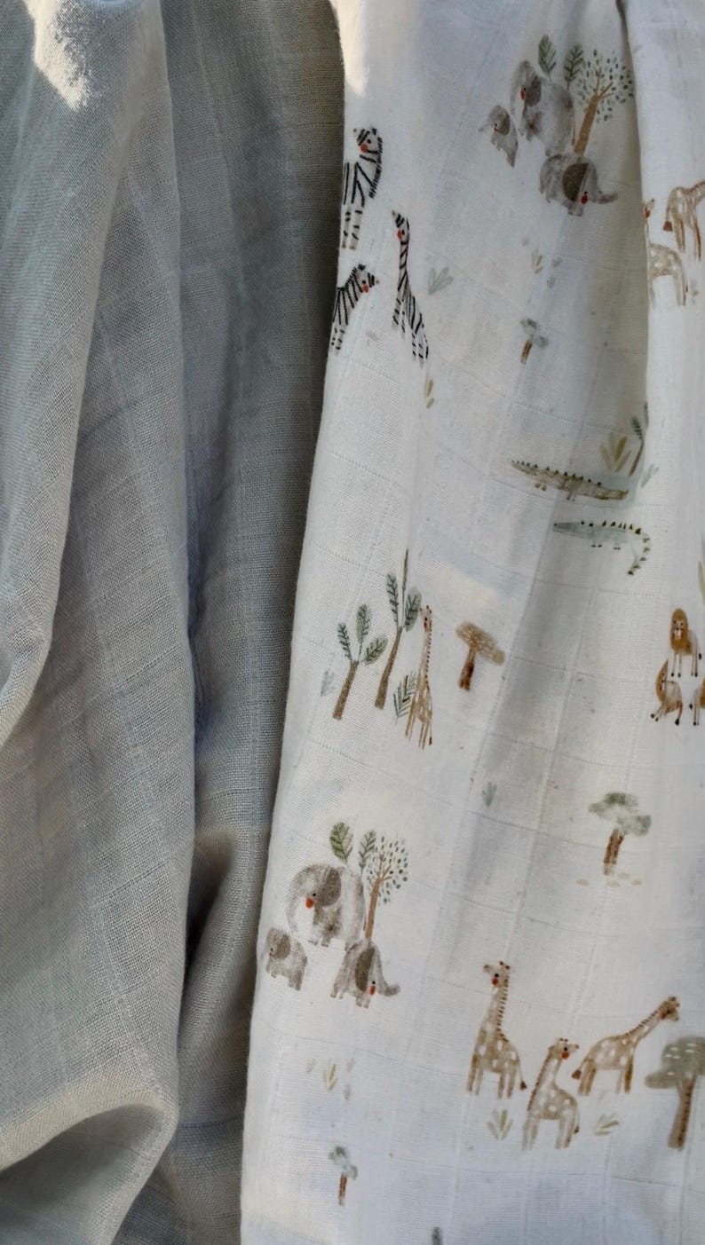 May include: A light blue muslin blanket with a safari animal print. The print features elephants, giraffes, zebras, and crocodiles in a naturalistic style. The blanket is soft and lightweight, ideal for a baby.