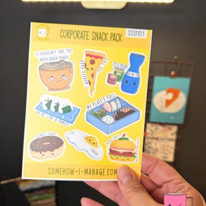 May include: A sheet of colorful stickers labeled "Corporate Snack Pack" featuring food-themed illustrations. Designs include ramen, pizza, sushi, a bento box, a donut, a fried egg, and a burger. The website SOMEHOW-I-MANAGE.COM is visible.