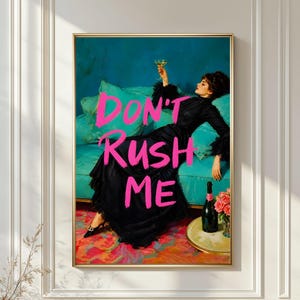 May include: A framed art print featuring a woman in a black dress reclining on a teal sofa, holding a glass of champagne. The words "DON'T RUSH ME" are written in bright pink across the image. A bottle of champagne and flowers are on a side table.