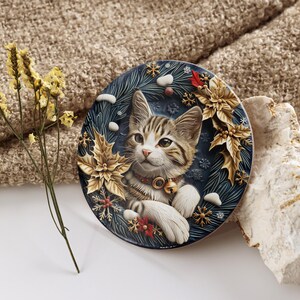 May include: A round decorative plate featuring a tabby cat with a festive collar and a bell. The plate has a dark blue background with gold poinsettias, snowflakes, and sprigs of evergreen. A sprig of dried yellow flowers is to the left.