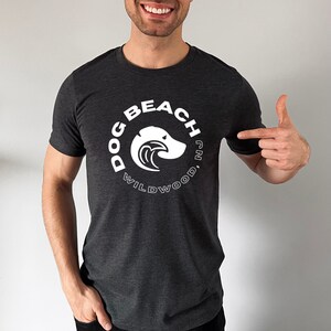 May include: A dark gray t-shirt with a white circle graphic that says "Dog Beach Wildwood, NJ" with a dog head and wave design inside the circle.
