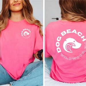 May include: Pink t-shirt with a white circle graphic on the front and back. The graphic says "Dog Beach Wildwood, NJ" and features a dog's head with a wave.