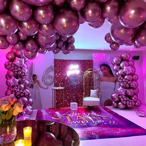 Puede incluir: Una fiesta de Sweet 16 con tem&aacute;tica morada y dorada con un tel&oacute;n de fondo de tela de lentejuelas, una jaula de p&aacute;jaros dorada y un arco de globos. El texto "An Evening of Stars Sweet 16 Ball" est&aacute; en el suelo.