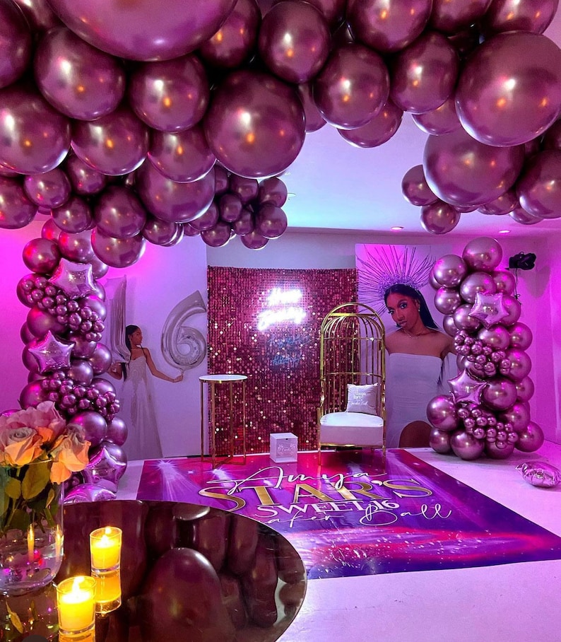 Puede incluir: Una fiesta de Sweet 16 con tem&aacute;tica morada y dorada con un tel&oacute;n de fondo de tela de lentejuelas, una jaula de p&aacute;jaros dorada y un arco de globos. El texto "An Evening of Stars Sweet 16 Ball" est&aacute; en el suelo.