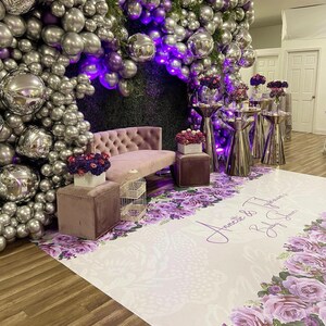 Puede incluir: Un tel&oacute;n de fondo blanco con globos morados y plateados, un sof&aacute; morado y un suelo con estampado floral con el texto "Annette & Typhonne Baby Shower" impreso en &eacute;l.