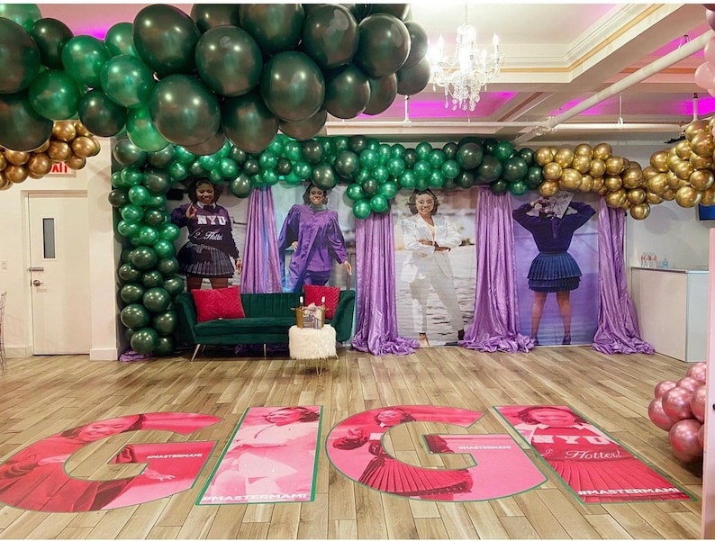 Puede incluir: Una sala de fiestas decorada con globos verdes y dorados, cortinas moradas y grandes letras rosas que deletrean "GIG" en el suelo. Las letras tienen im&aacute;genes de mujeres con diferentes atuendos y el texto "#HASTEMANHI" y "Hotter!" en ellas.