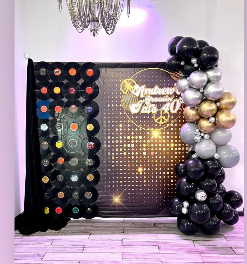 Puede incluir: Un tel&oacute;n de fondo negro y dorado con un dise&ntilde;o de bola de discoteca y el texto "Andrew Groovin' Into 40". Un arco de globos negro, plateado y dorado se encuentra en el lado derecho de la imagen.