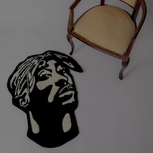 Può includere: Tappeto bianco e nero con un ritratto di una persona con una bandana. Il tappeto è su una superficie bianca.