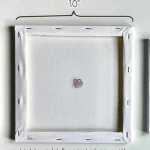 May include: Back view of a square canvas art piece, measuring 10 inches across. The canvas is stretched over a wooden frame and stapled in place. The text "BACK VIEW OF CRAPPY CAKE ART" is at the top, with additional text at the bottom. A small sticker is affixed to the canvas.