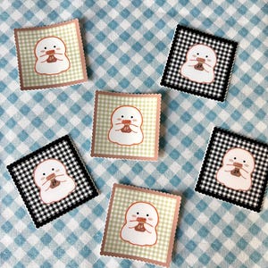 May include: Square stickers with a cartoon character holding a bottle. The stickers have a scalloped edge and are set on a blue and white checkered background. Some stickers have a black and white checkered pattern, while others have a light green and white checkered pattern.