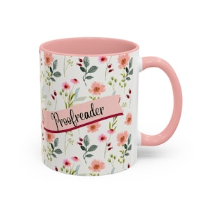 May include: A white ceramic mug with a pink floral pattern and a pink interior. The mug has a pink handle and the word "Proofreader" written on a pink banner.