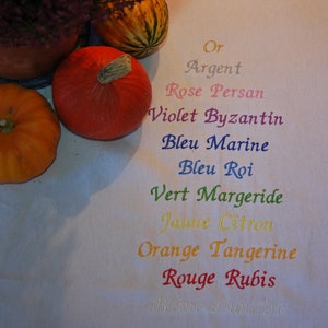 une serviette de table blanche sur laquelle 11 noms de couleurs sont brodés, correspondant aux couleurs que vous pouvez choisir pour vos broderies : or, argent, rose, violet, marine, bleu roi, vert, jaune, orange, rouge, blanc.