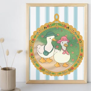 Puede incluir: Una lámina artística enmarcada con dos patos blancos dentro de un marco ovalado dorado decorativo. Un pato lleva un sombrero y un bolso verdes, mientras que el otro lleva un sombrero y un pañuelo rosas. El fondo tiene rayas verticales azul claro y blancas.