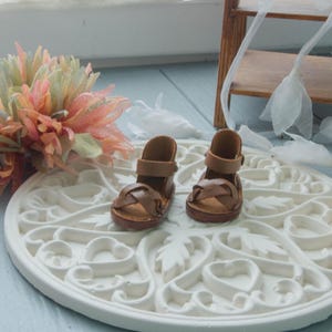 Peut inclure: Une paire de sandales en cuir marron avec une boucle de fermeture. Les sandales sont sur une surface décorative blanche.