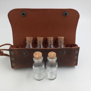 Puede incluir: Una bolsa de cuero marr&oacute;n con seis peque&ntilde;as botellas de vidrio con tapones de corcho. La bolsa tiene una solapa que se abre para revelar las botellas.