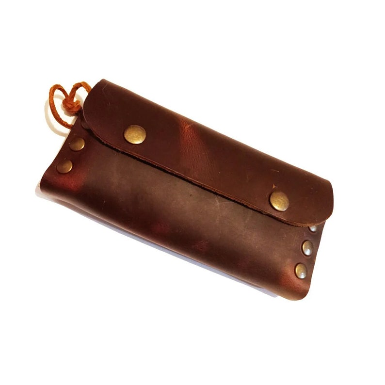 Puede incluir: Una cartera de cuero marr&oacute;n con cierre de solapa y detalles met&aacute;licos. La cartera tiene un aspecto desgastado y se asegura con un broche met&aacute;lico.