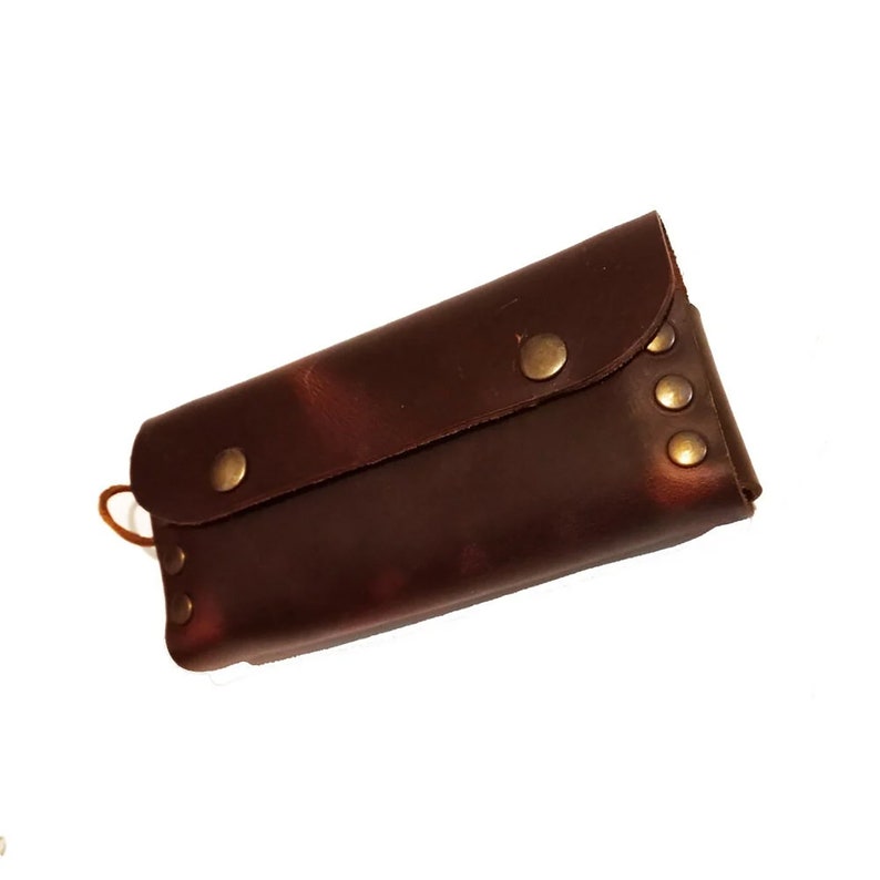 Puede incluir: Una cartera de cuero marr&oacute;n con cierre de solapa y tachuelas met&aacute;licas. La cartera tiene un aspecto desgastado y est&aacute; cerrada.