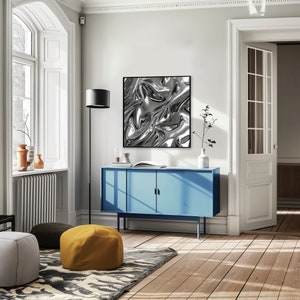 May include: A blue cabinet with two doors and a silver abstract art print hanging above it. The cabinet is in a room with a large window and a wooden floor.