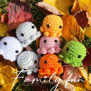 May include: A collection of crocheted octopus plushies in various colors, including white, gray, pink, orange, and green. The plushies are arranged on a bed of autumn leaves.