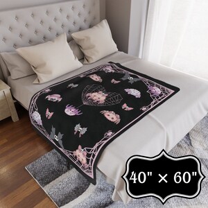 May include: A black and pink fleece throw blanket with a spiderweb design and cute cartoon spiders. The blanket is 40 inches by 60 inches.