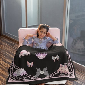 May include: A black fleece throw blanket with a pink spiderweb design and pink cartoon spiders. The blanket features a skull and crossbones design on the butterflies and spiders.