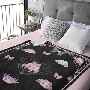 May include: A black and pink fleece throw blanket with a spiderweb design and cute cartoon spiders. The spiders are wearing bows and have skulls on their heads.