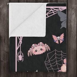 May include: A black and pink fleece throw blanket with a cute spider, butterfly, and spiderweb pattern.