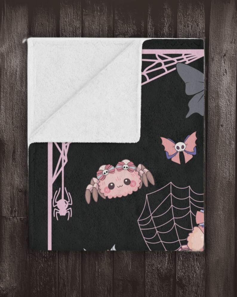 May include: A black and pink fleece throw blanket with a cute spider, butterfly, and spiderweb pattern.