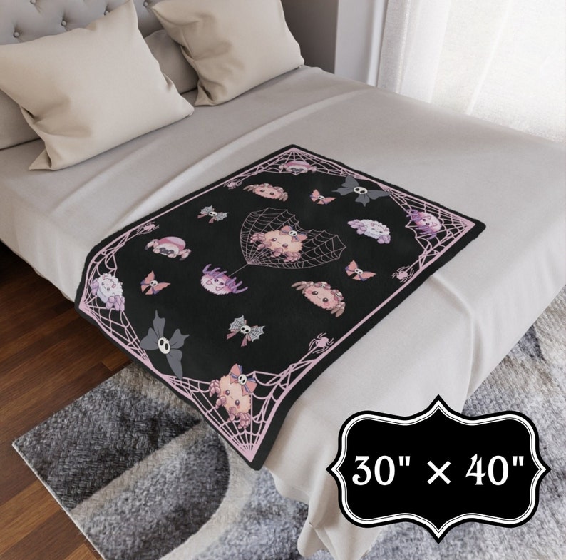 May include: A black and pink throw blanket with a spiderweb design and cute spider illustrations. The blanket is 30 inches by 40 inches.