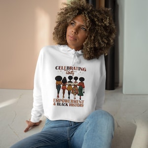 Op de afbeelding: Witte hoodie met een afbeelding van vijf zwarte vrouwen die samen staan. De tekst "Celebrating Unity Empowerment & Black History" staat op de hoodie gedrukt.