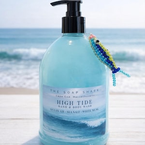 May include: A light blue bottle of High Tide hand and body wash from The Soap Shark, Cape Cod, Massachusetts. The bottle has a black pump and a label with ocean-themed text. A beaded fish decoration is attached to the bottle.