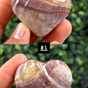 May include: A heart-shaped stone with a mix of purple, white, and gold colors. The stone has a polished surface and a natural, swirled pattern. A small white sticker with the number "12Y" is attached to the stone. The image also includes the text "#1".