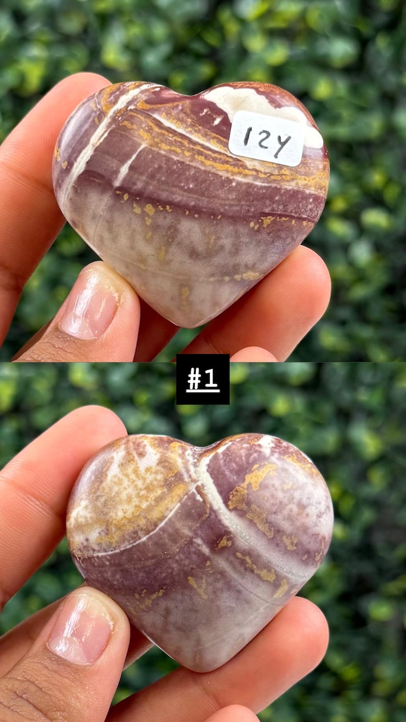May include: A heart-shaped stone with a mix of purple, white, and gold colors. The stone has a polished surface and a natural, swirled pattern. A small white sticker with the number "12Y" is attached to the stone. The image also includes the text "#1".