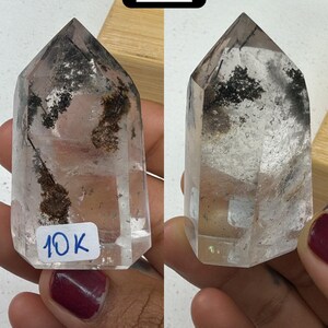 May include: Two clear quartz crystal points with dark inclusions and a hexagonal shape. One has a sticker with "10K" written on it. The crystals are held in a person's hand. The image also includes a black square with the number "#4" in white.