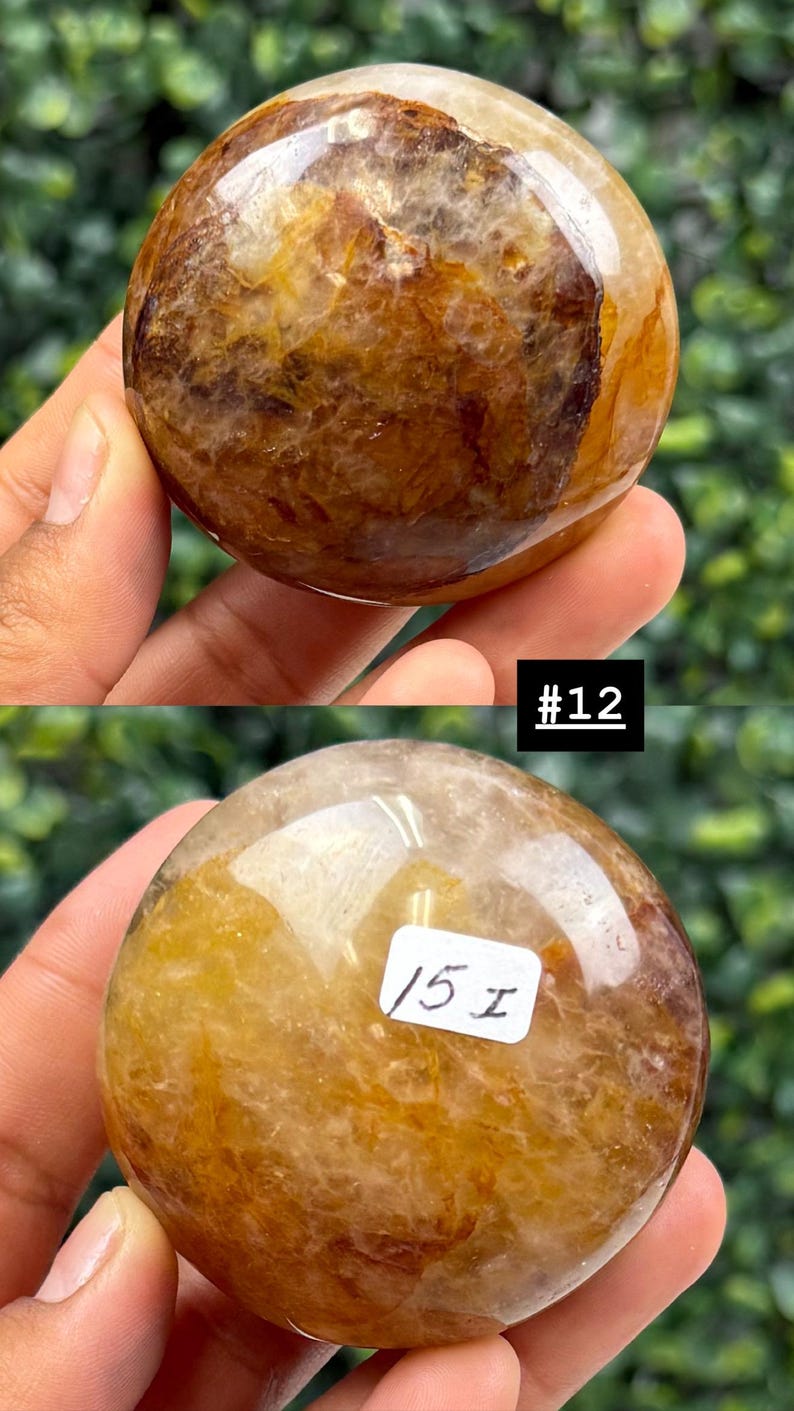 May include: Two polished, spherical gemstones with a mix of golden, brown, and translucent hues. The top stone has the text "#12" in a black rectangle. The bottom stone has the text "15 I" on a white rectangle. The stones are held in a hand.
