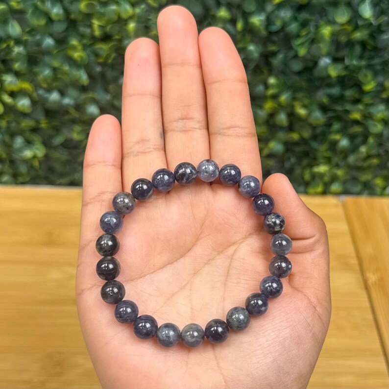 May include: A beaded bracelet featuring dark blue and gray spherical beads. The bracelet is held in a hand, showcasing the polished, smooth texture of the stones. The beads have a speckled appearance, adding visual interest to the jewelry.