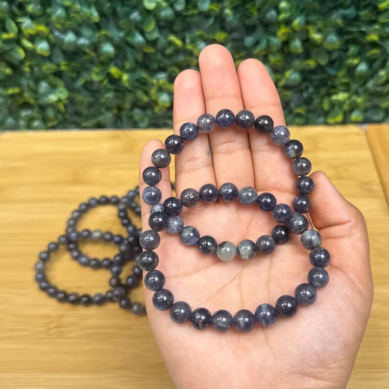 May include: Several dark blue beaded bracelets. The bracelets are made of round, polished beads with a mix of dark blue and gray tones. The bracelets are displayed on a light wooden surface.