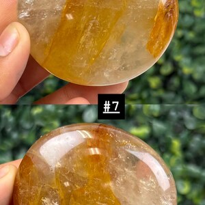 May include: Two polished, round gemstones with a golden-yellow and clear appearance. The stones have a smooth, reflective surface. One stone has the text "13 c" on a white label. The other stone has the text "#7" on a black label.
