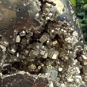 May include: Close-up of a pyrite specimen, showcasing a cluster of metallic, cubic crystals. The crystals have a reflective, golden-bronze hue, contrasting with the darker, rough matrix. The overall texture is jagged and irregular.